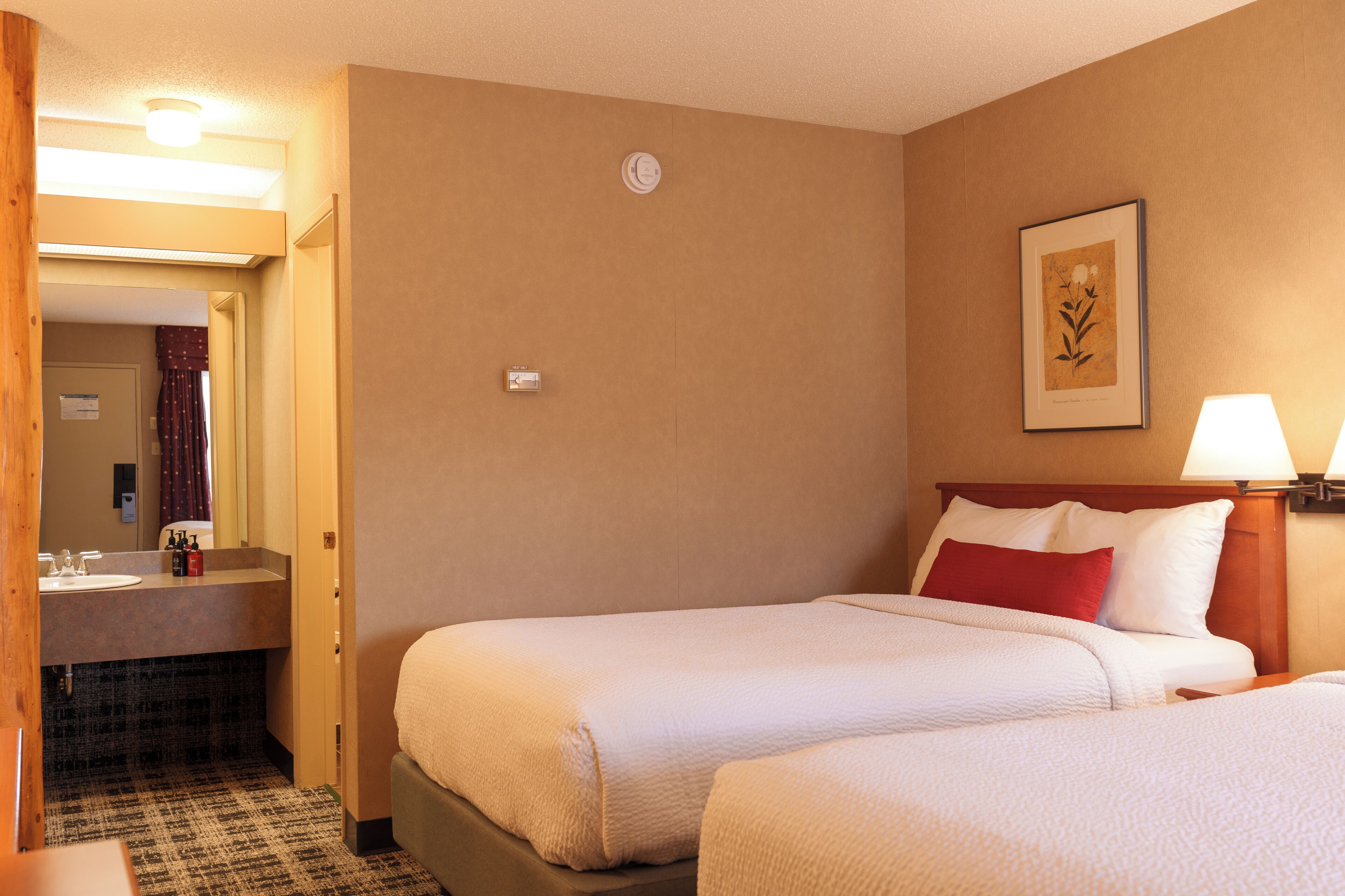 A hotel room with two beds, a bathroom, and a framed picture on the wall.