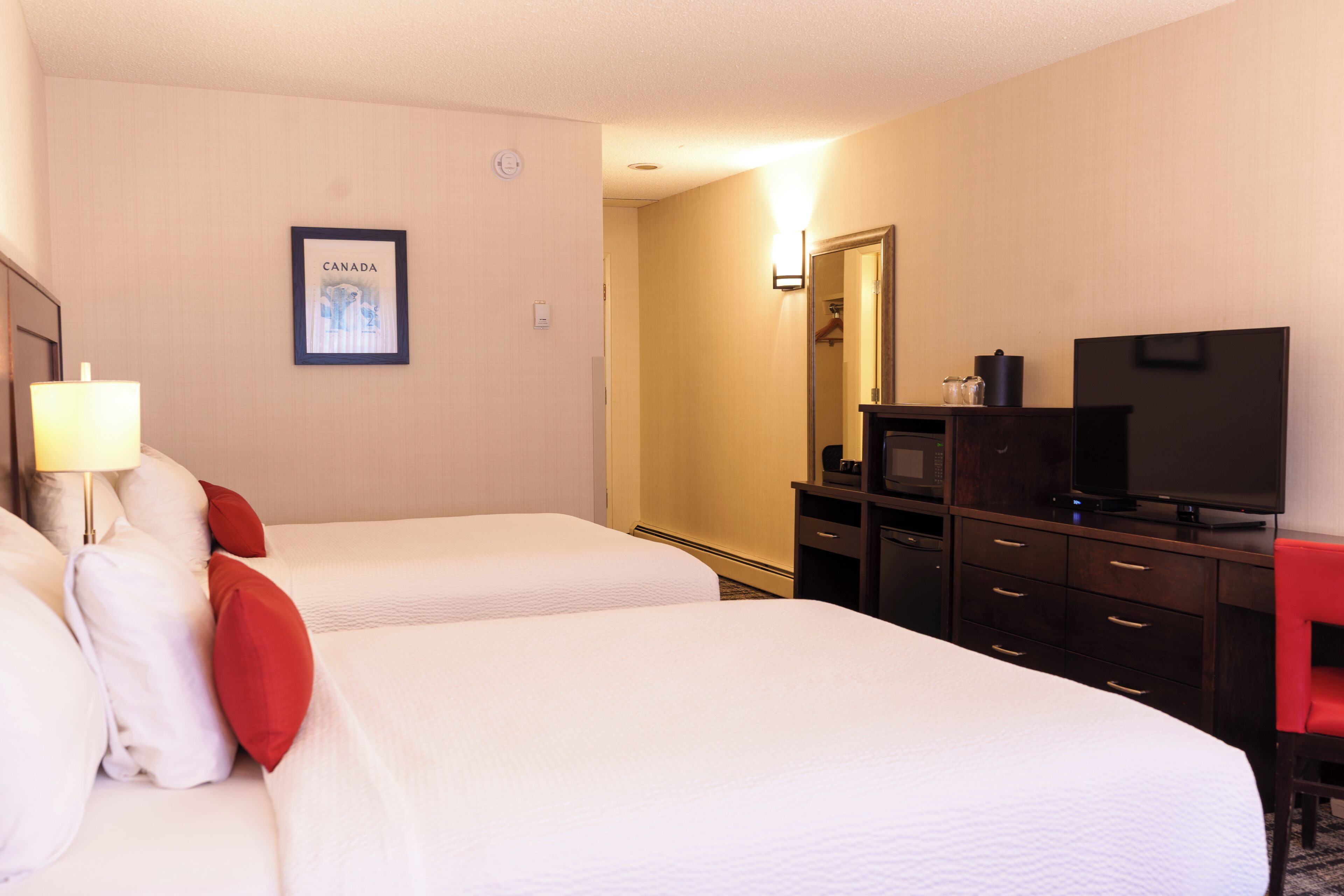 Een hotelkamer met twee bedden, een televisie, een dressoir en een ingelijst schilderij aan de muur.