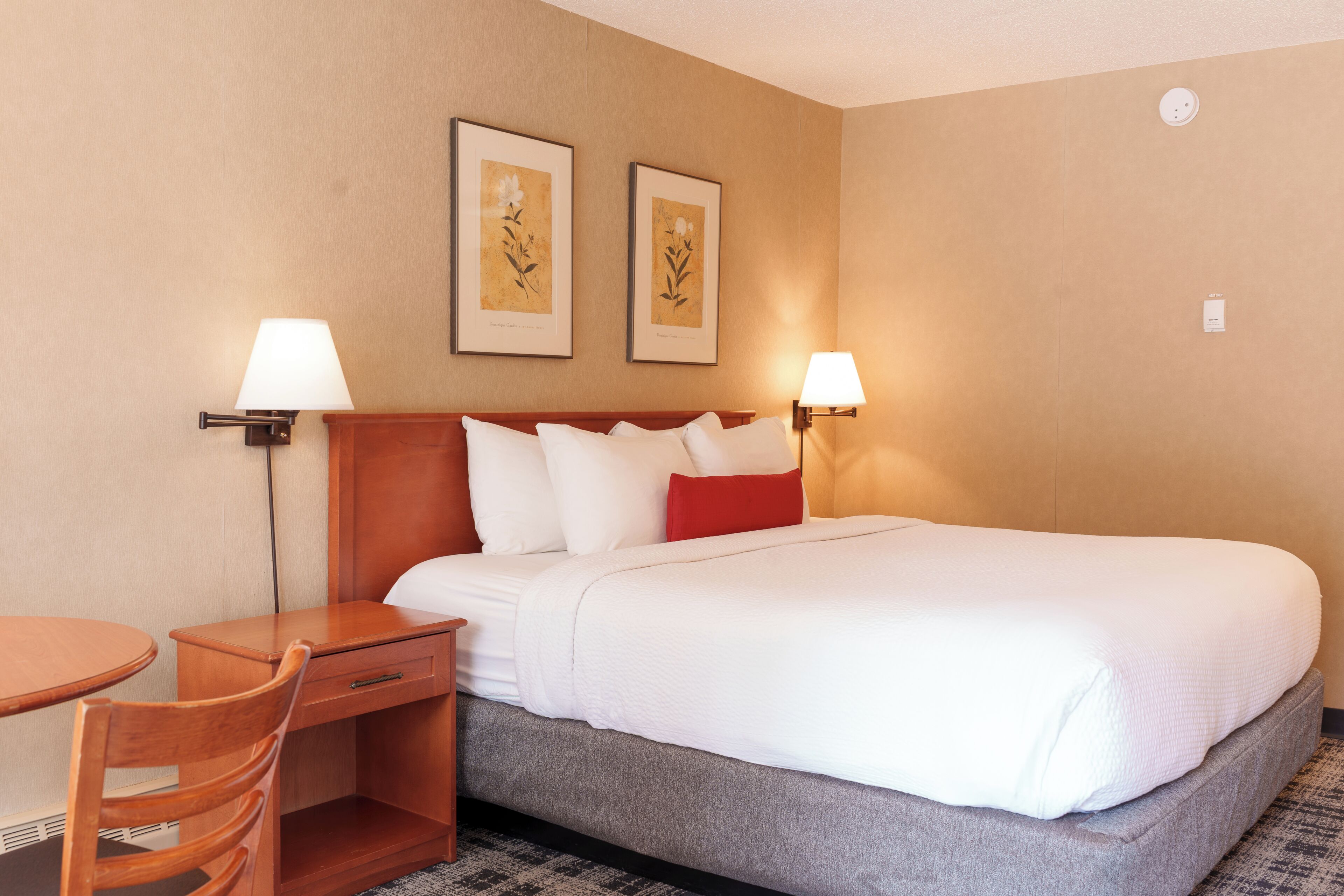 A hotel room with a bed, two bedside lamps, a desk, and a chair.