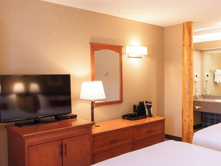 A hotel room with a flat-screen TV, a lamp, a coffee maker, a mirror, and a bed.