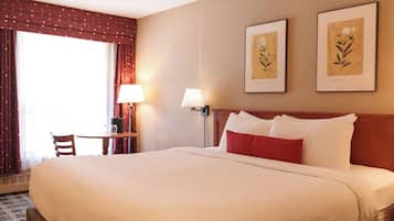 Habitación de hotel con una cama grande, un escritorio con silla, una lámpara y dos láminas botánicas enmarcadas en la pared.