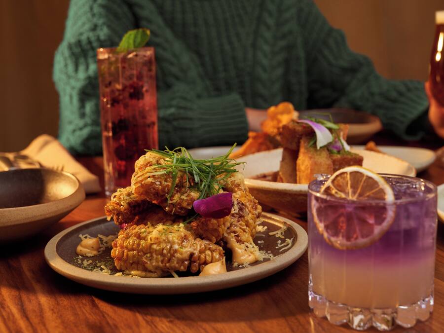 A dining table with various dishes, a tall glass of a purple drink, and a person in a green sweater.