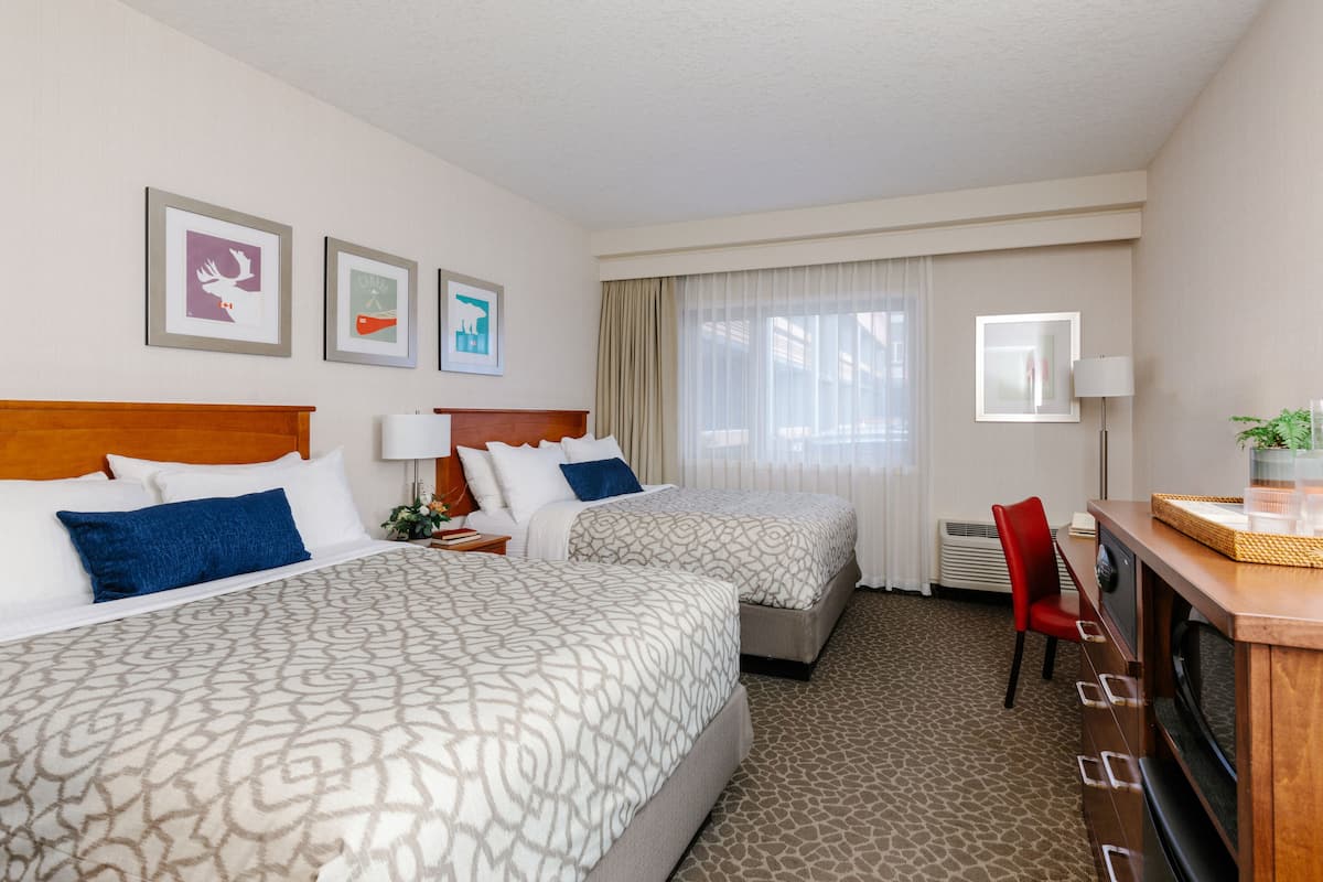 A hotel room with two beds, a desk with a lamp, a chair, and a television.