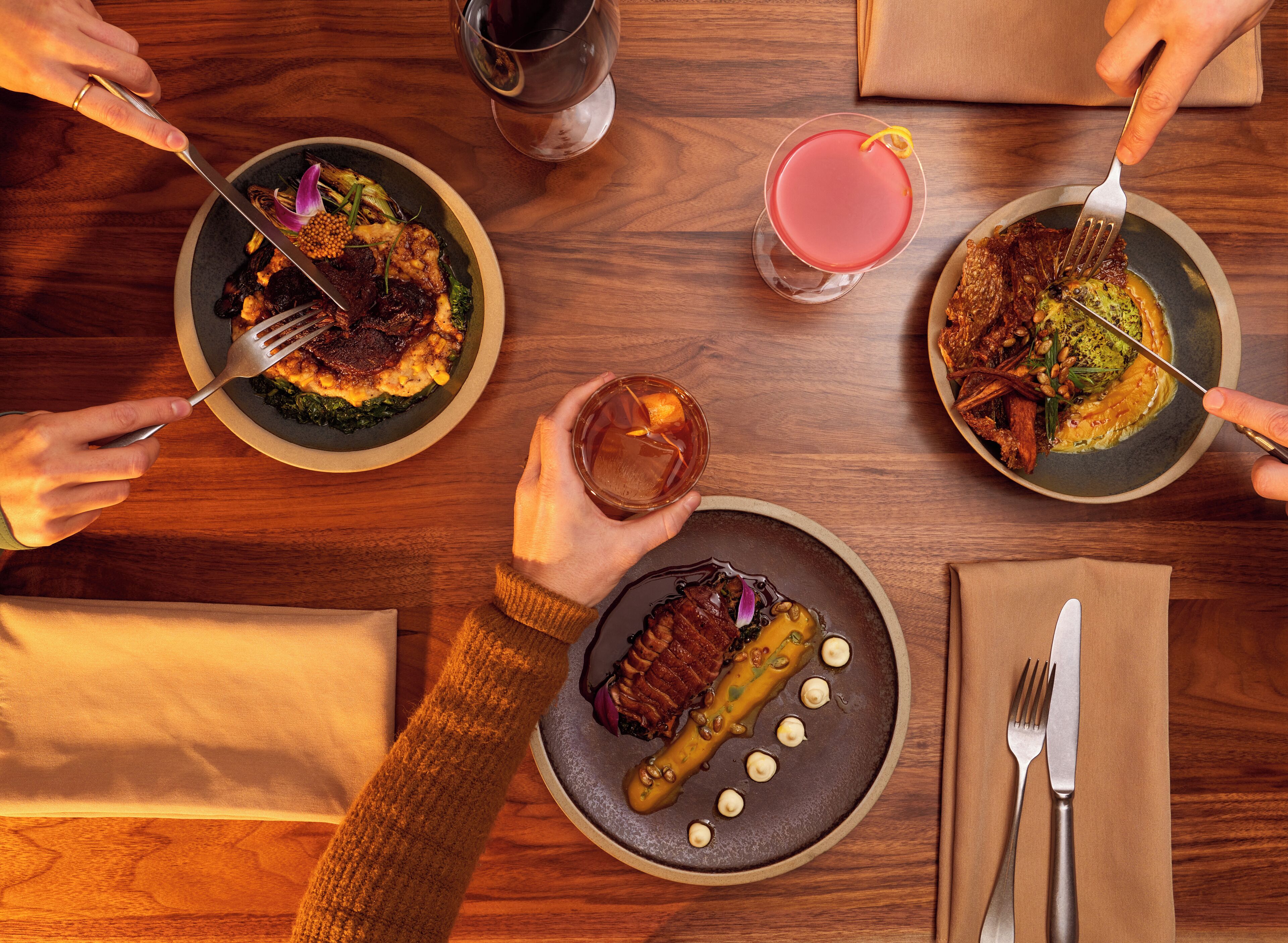 Une table à manger avec des assiettes remplies de nourriture, des couverts et des verres contenant des boissons.