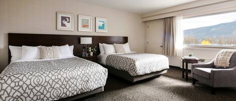 A hotel room with two beds, a chair, a nightstand, and a window with a mountain view.