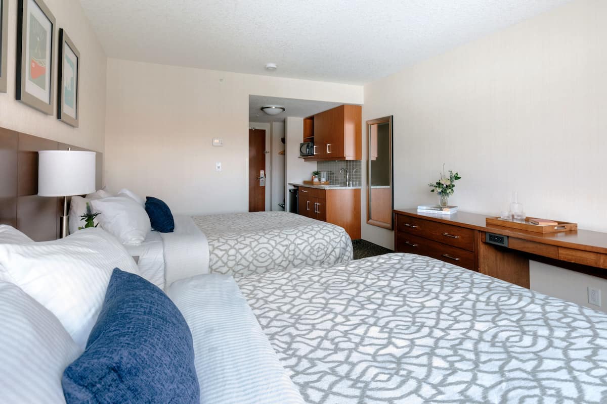 A hotel room with two beds, a kitchenette, and a bathroom.