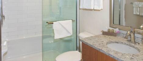Un baño moderno con ducha de vidrio, inodoro blanco y lavamanos sobre encimera de granito.
