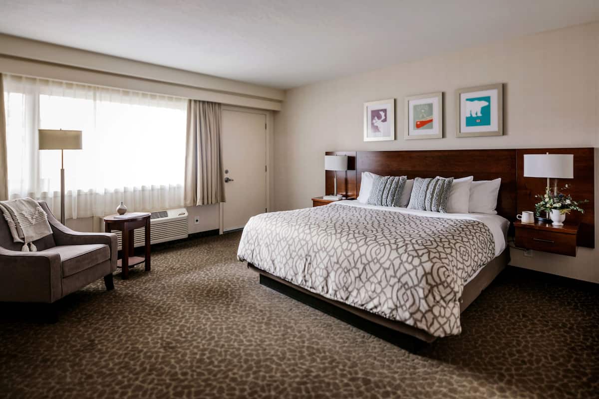 A hotel room with a large bed, a chair, a desk, and a lamp. There are three framed pictures on the wall.