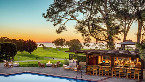 Un bar junto a la piscina con asientos exteriores, piscina y vistas a un campo de golf al atardecer.