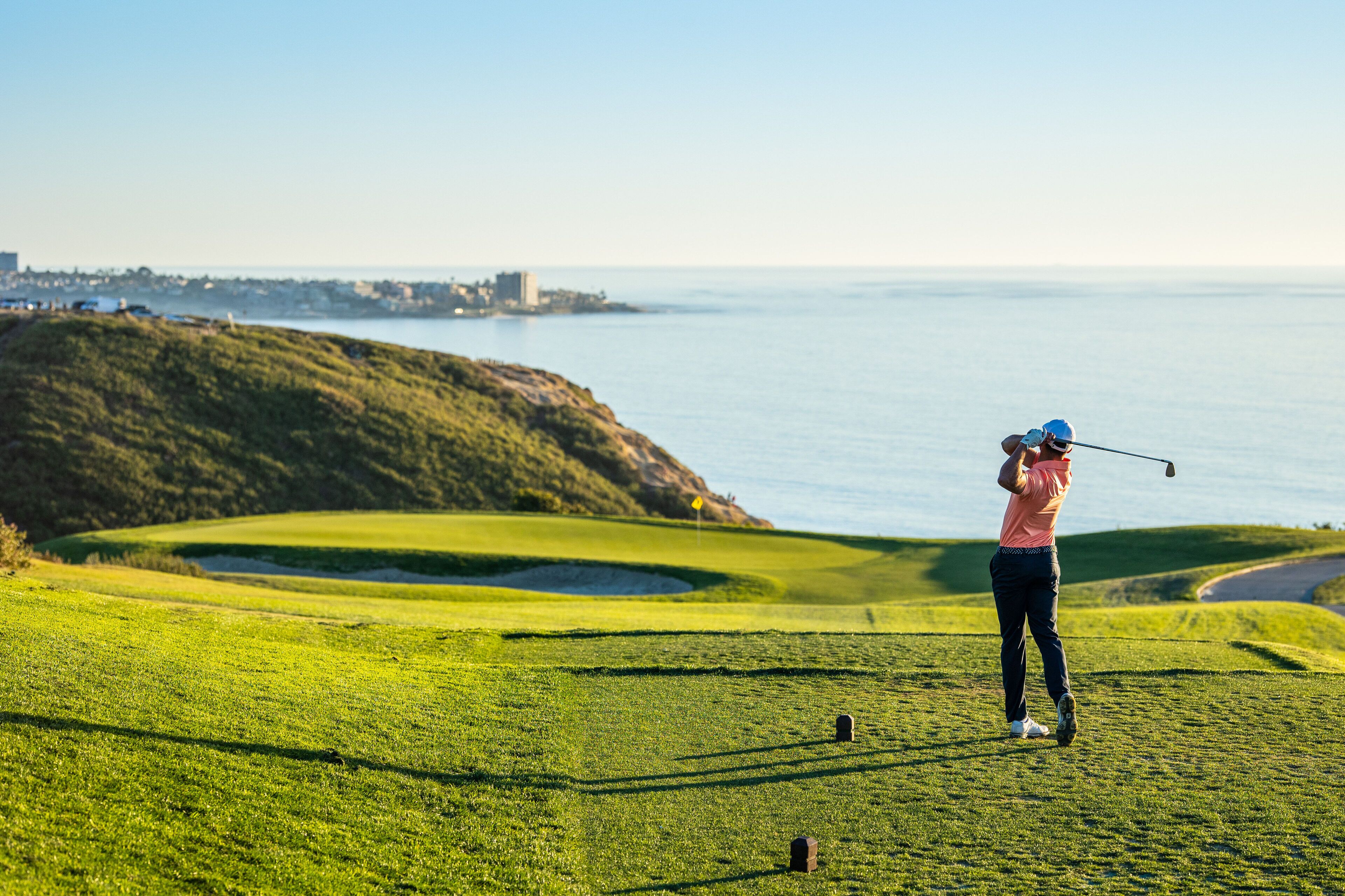 A golf course with a view of the ocean and a distant city skyline.