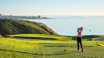 A golf course with a view of the ocean and a distant city skyline.