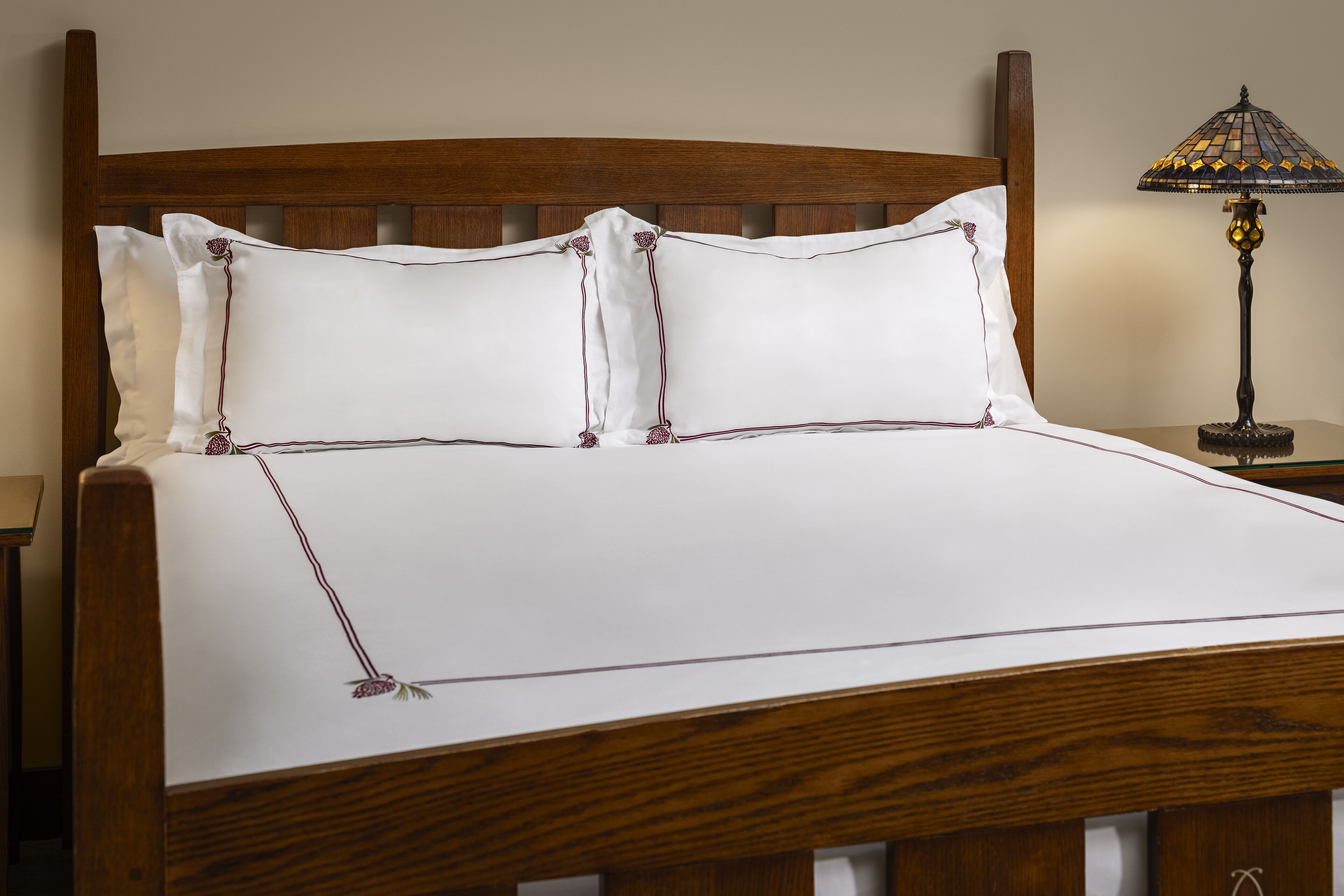 Una cama bien hecha con cabecera de madera, ropa de cama blanca y una lámpara decorativa en la mesita de noche.