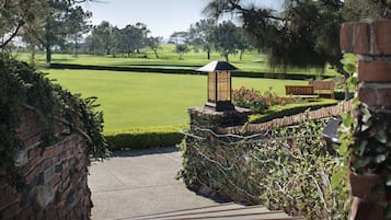 A brick wall with a stone lantern and a bench overlooking a well-manicured lawn with a golf course in the distance.