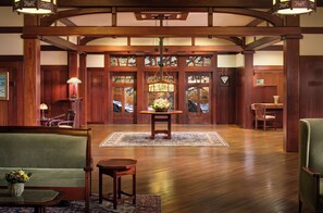 A lobby with wooden flooring, a central table with a floral arrangement, a green sofa, and a wooden bench.
