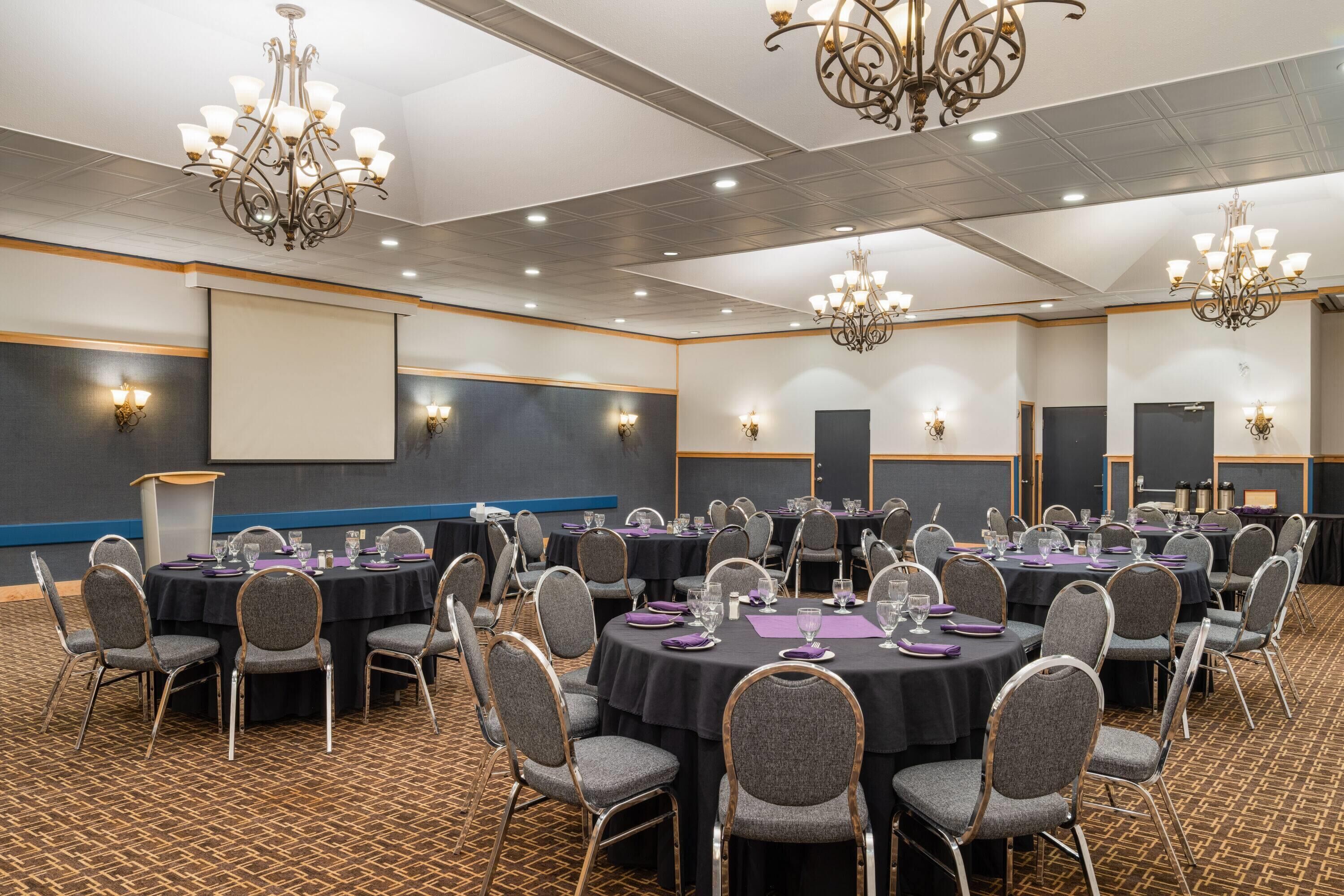 A conference room with round tables, grey chairs, and chandeliers.