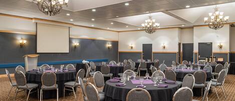 A conference room with round tables, grey chairs, and chandeliers.