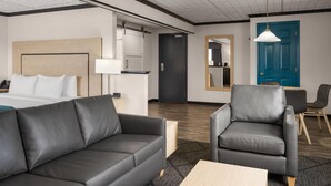 A hotel room with a bed, a black leather sofa, a grey armchair, a small table, a lamp, a mirror, a blue door, and a wooden ceiling. - Sternwheeler Hotel & Conference Centre, Trademark by Wyndham (Whitehorse)