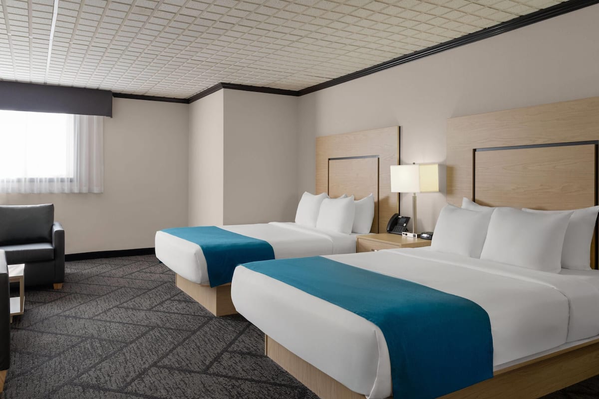 A hotel room with two beds, a desk, a chair, and a window with curtains.