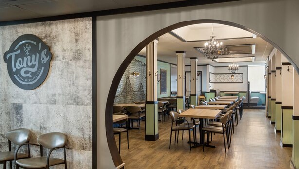 A restaurant interior with a long counter, wooden flooring, and a large arched doorway. - Sternwheeler Hotel & Conference Centre, Trademark by Wyndham (Whitehorse)