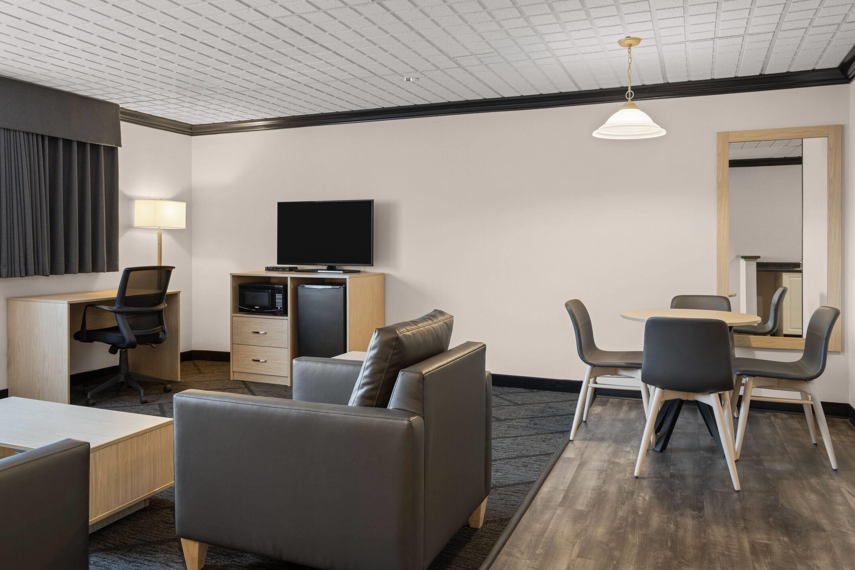 Ein Hotelzimmer mit Flachbildfernseher, Schreibtisch mit Lampe, Sofa, Esstisch mit Stühlen und einem großen Spiegel.