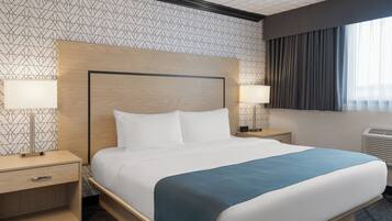 A hotel room with a large bed, two bedside tables with lamps, a headboard, and a window with curtains.