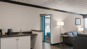 A compact hotel room with a kitchenette, a sofa, a bedside table, and a lamp. - Sternwheeler Hotel & Conference Centre, Trademark by Wyndham (Whitehorse)