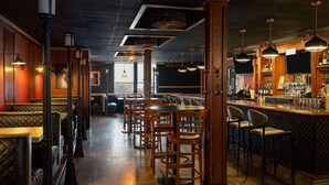 A bar area with wooden bar stools, a counter with bottles, and pendant lighting. - Sternwheeler Hotel & Conference Centre, Trademark by Wyndham (Whitehorse)