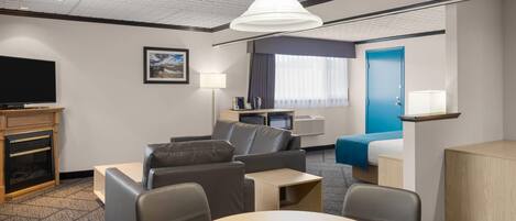 A modern hotel room with a flat-screen TV, a sofa, a dining table, a coffee table, a lamp, and a blue door.