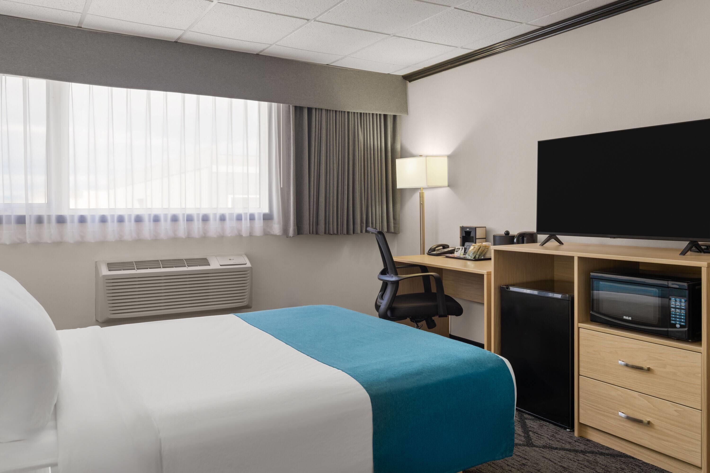 A hotel room with a bed, a desk with a computer, a TV, and a microwave.