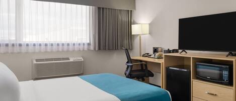 A hotel room with a bed, a desk with a computer, a TV, and a microwave.