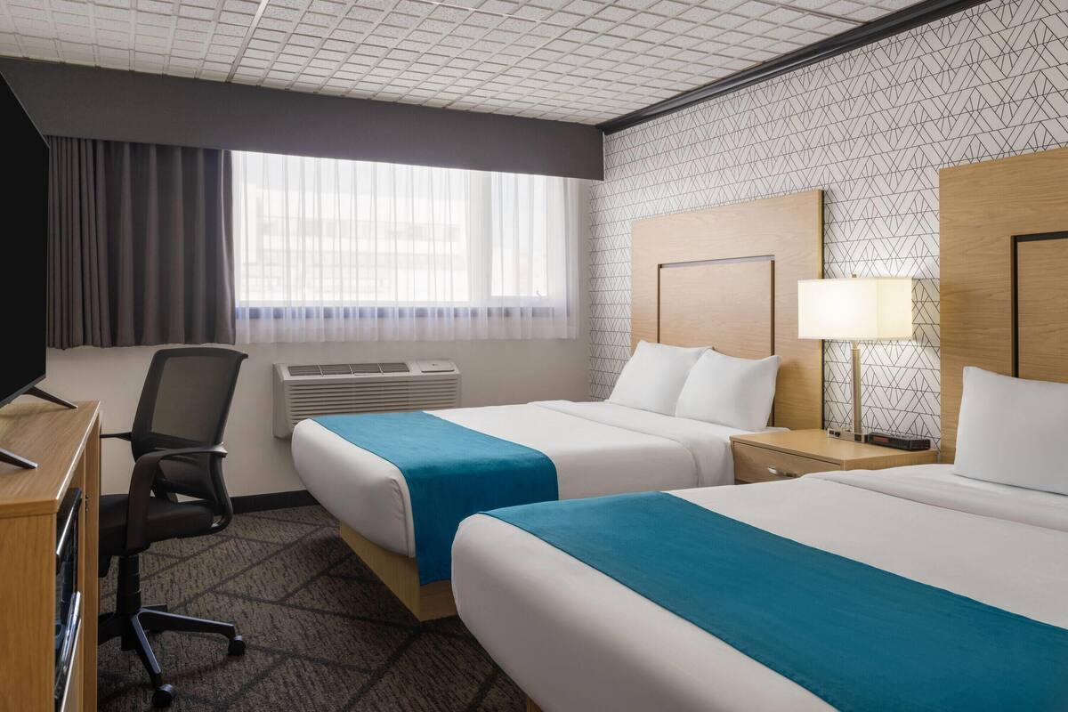 A hotel room with two beds, a desk, a chair, a lamp, and a window with curtains.