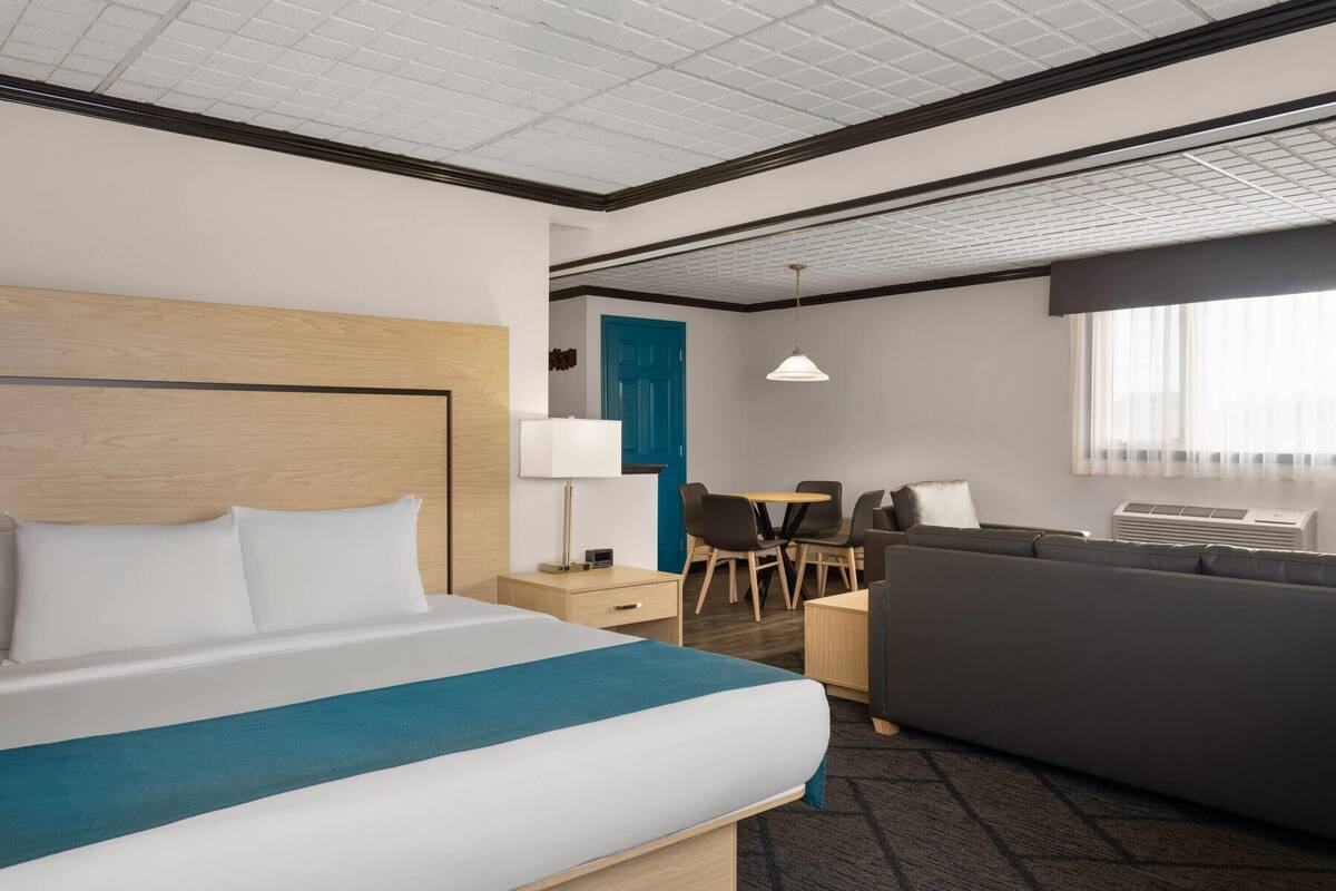 A hotel room with a bed, a desk, a sofa, and a dining area.