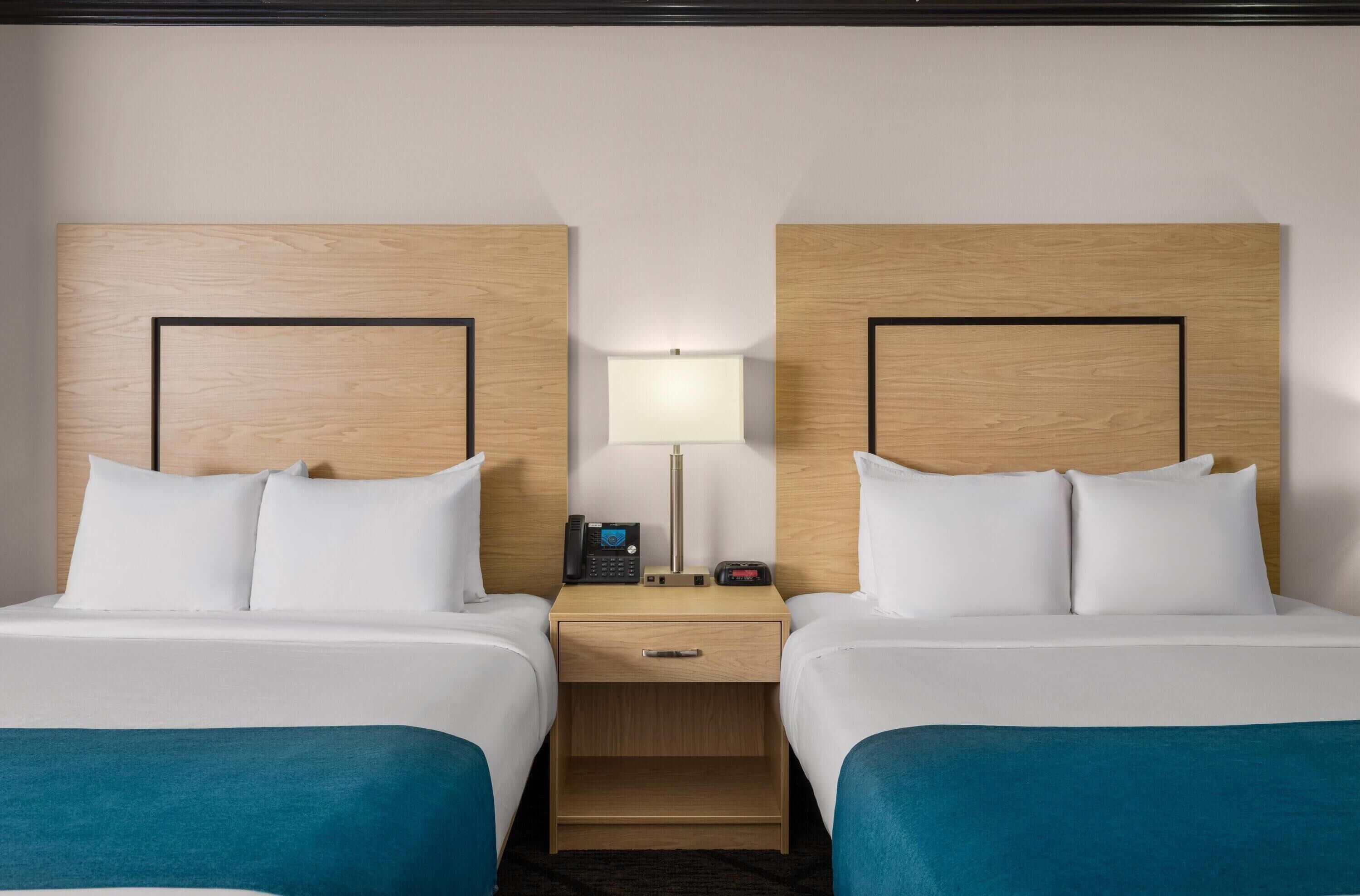 A hotel room with two beds, a nightstand with a lamp, and a phone.