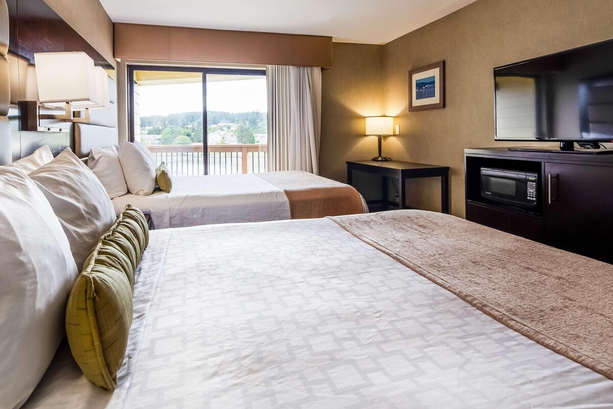 A hotel room with two beds, a TV, a desk, and a balcony with a view.