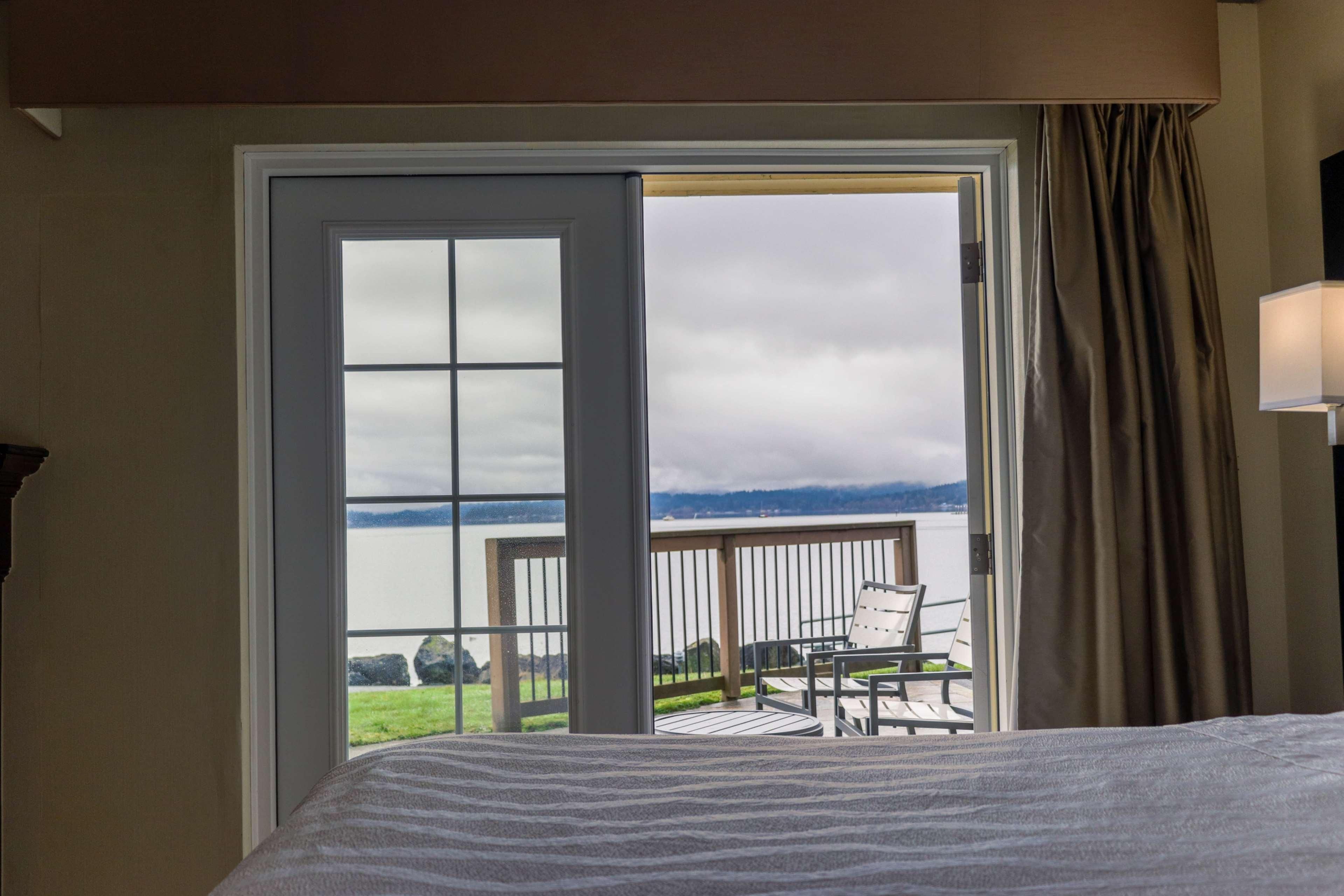 A hotel room with a bed, a view of a balcony with a table and chairs, and a large window.