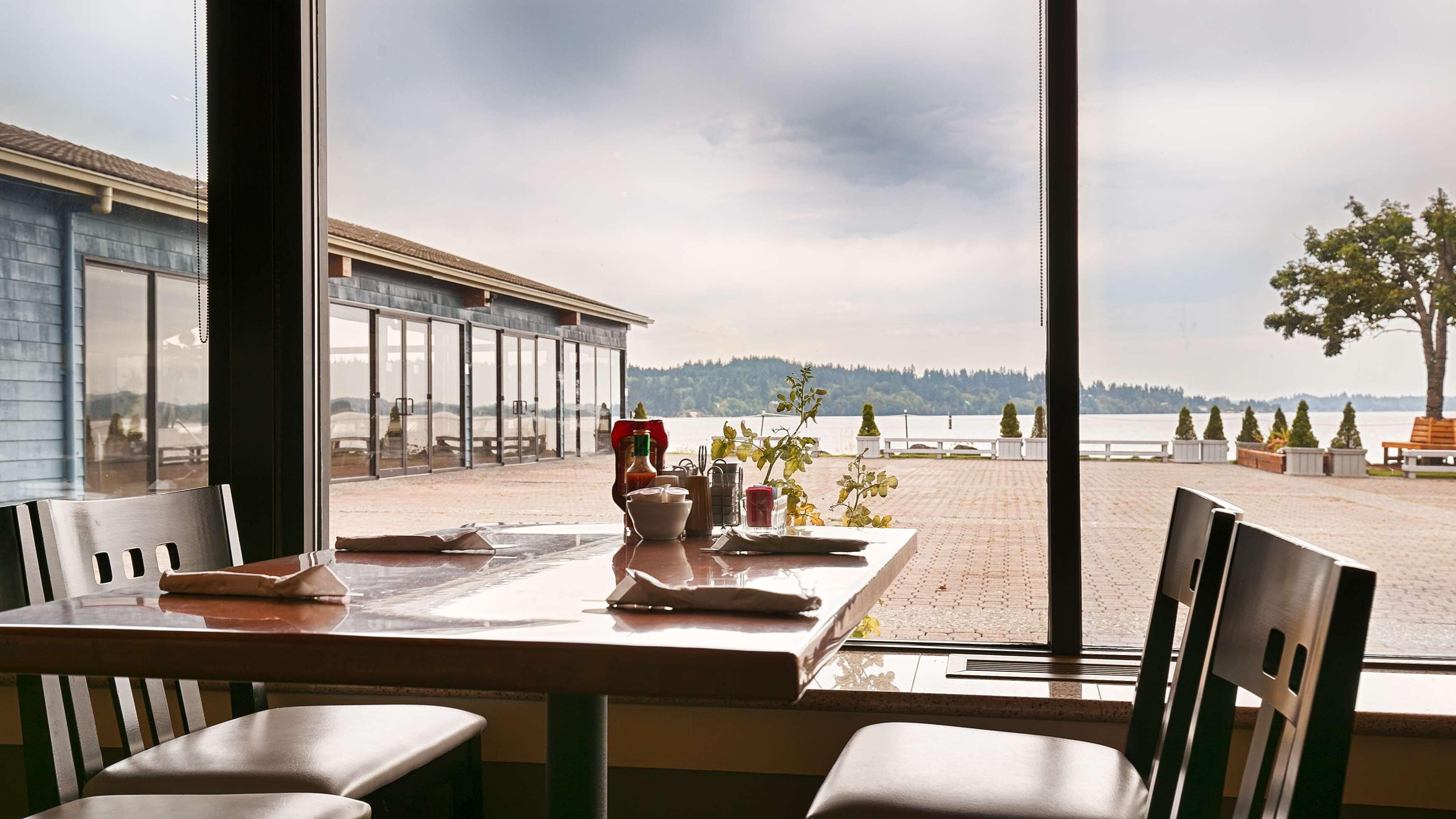 Een eetgedeelte met een tafel gedekt voor twee, met uitzicht op een strand en een panorama van water en heuvels in de verte.