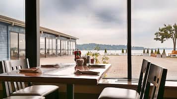 Un comedor con una mesa dispuesta para dos, con vista a una playa y colinas lejanas.