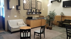 Un espacio habitable compacto con sofá, una mesa de comedor con sillas, una pequeña cocina con microondas y una planta en maceta.