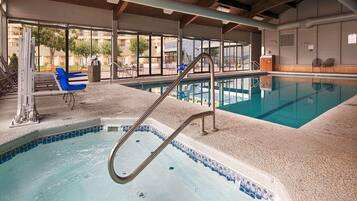 An indoor swimming pool with a diving board, a no smoking sign, and a view of a residential area through large windows.