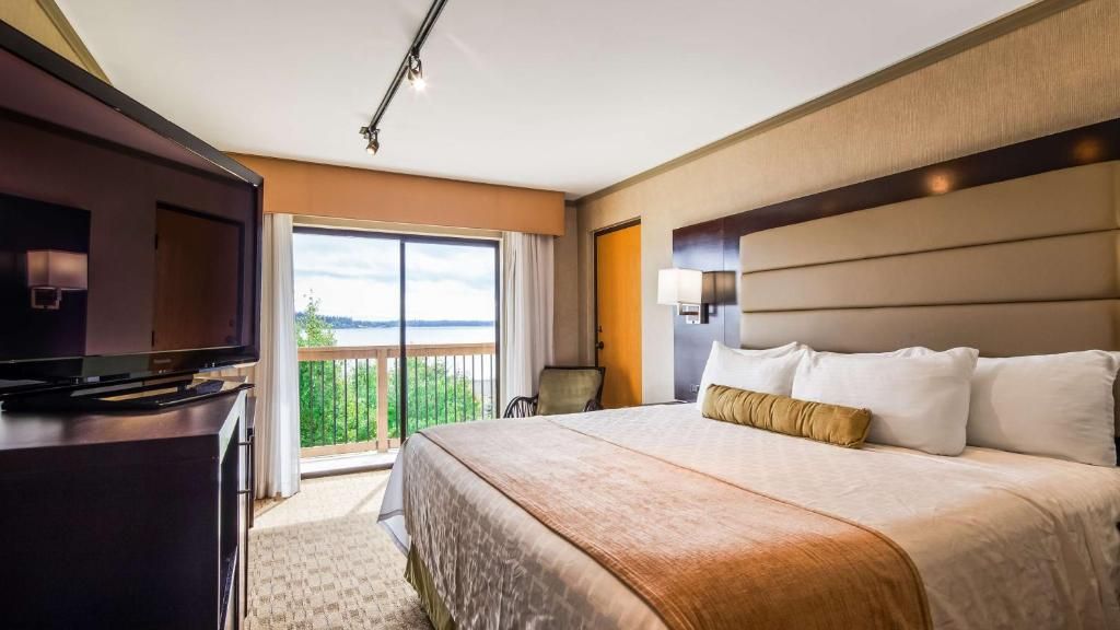 A hotel room with a large bed, a television, a desk, and a balcony with a view.