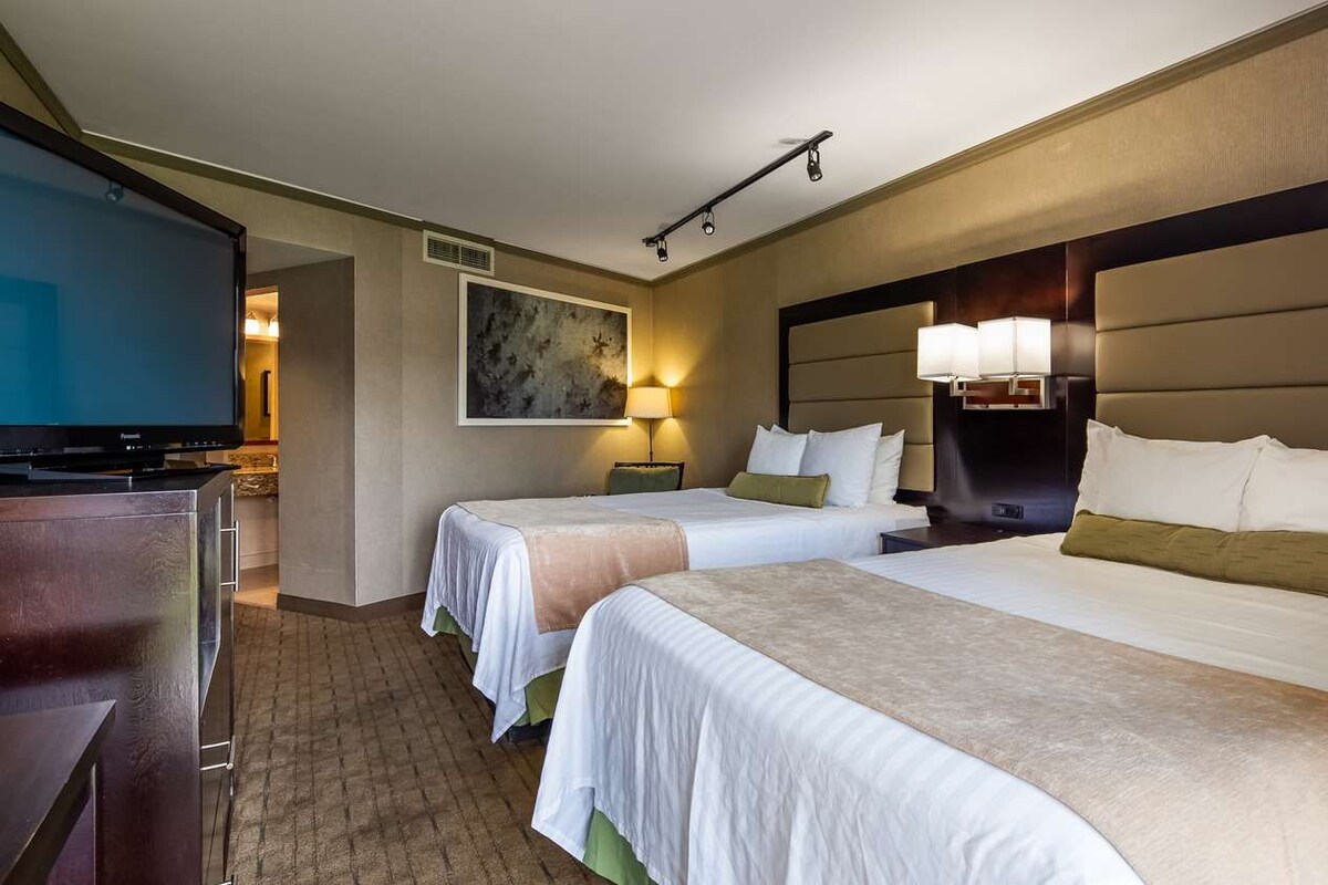 A hotel room with two beds, a TV, a painting, and a lamp.