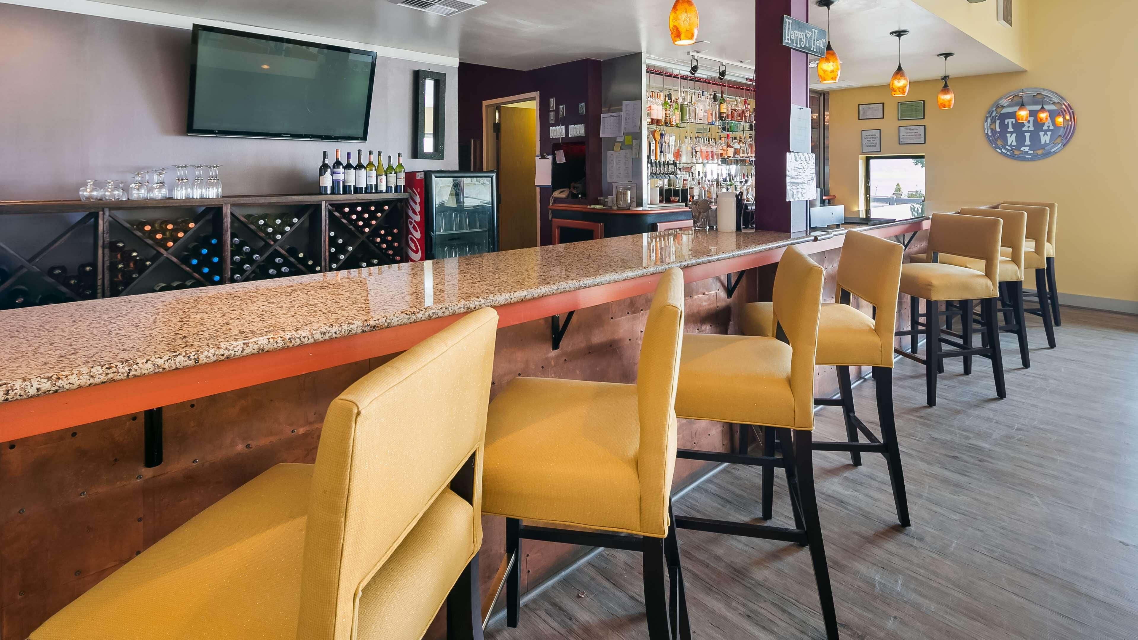 A bar area with a long counter, multiple seating options, and a television mounted on the wall.
