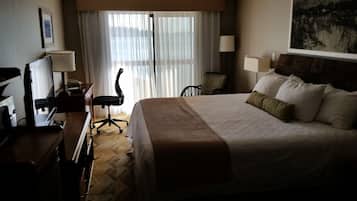 A hotel room with a large bed, a desk with a chair, a lamp, and a window with curtains.