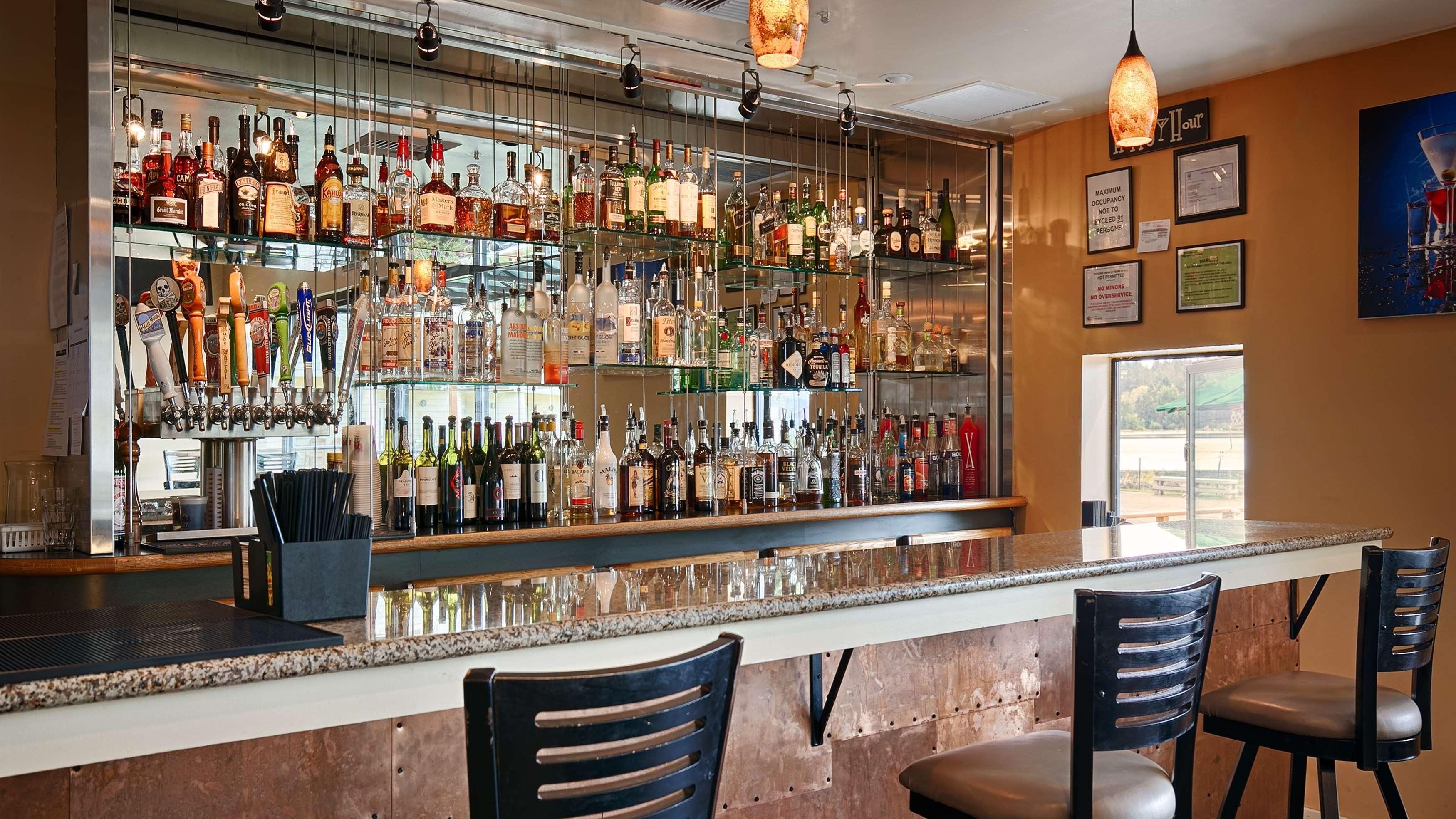 A bar with a variety of liquor bottles and a selection of beer taps. There are two chairs at the bar.