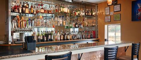 A bar with a variety of liquor bottles and a selection of beer taps. There are two chairs at the bar.