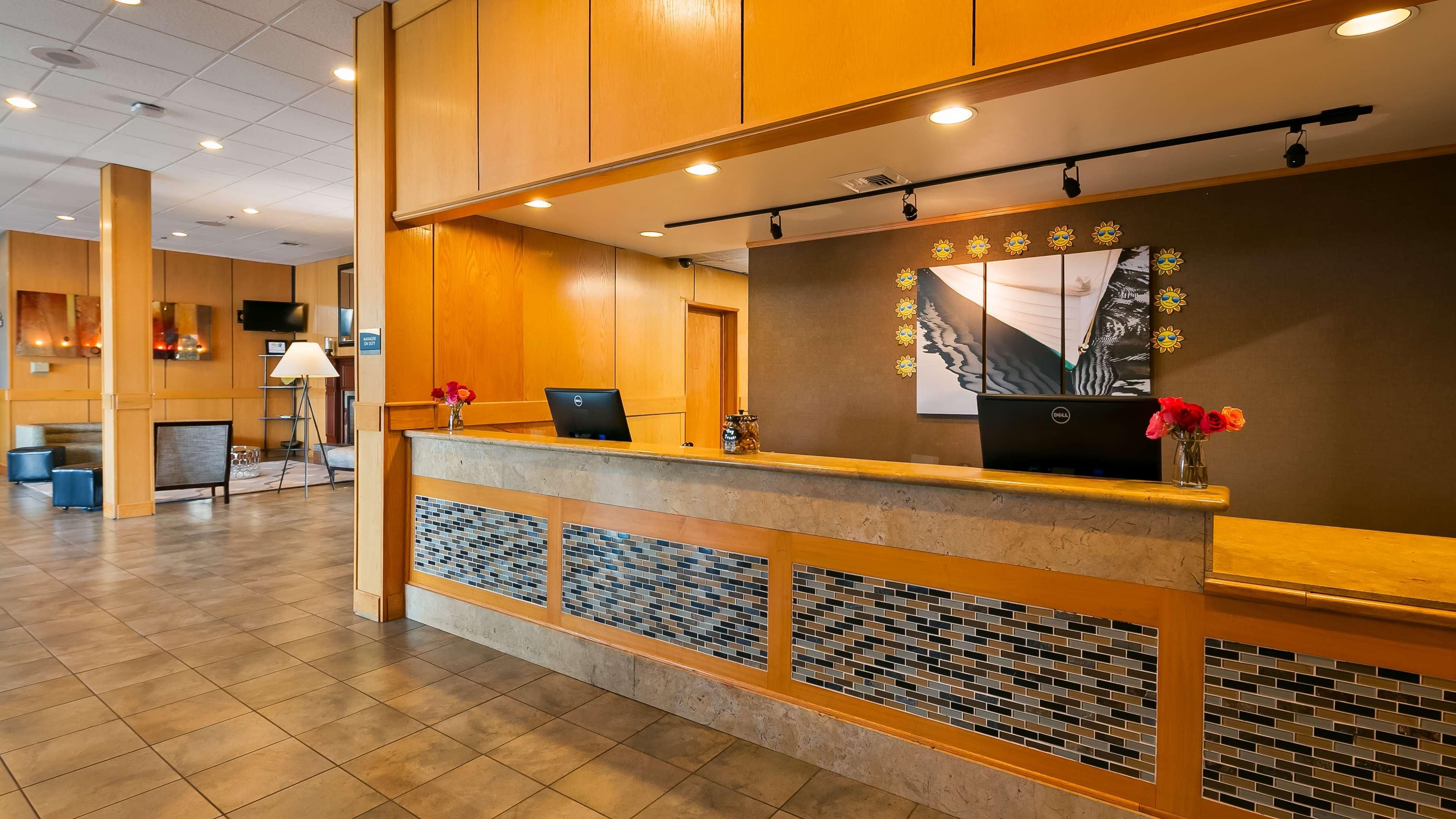 A hotel reception area with a wooden reception desk, a Dell computer, and a vase of flowers.