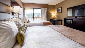 A hotel room with two beds, a TV, a desk, and a balcony with a view.