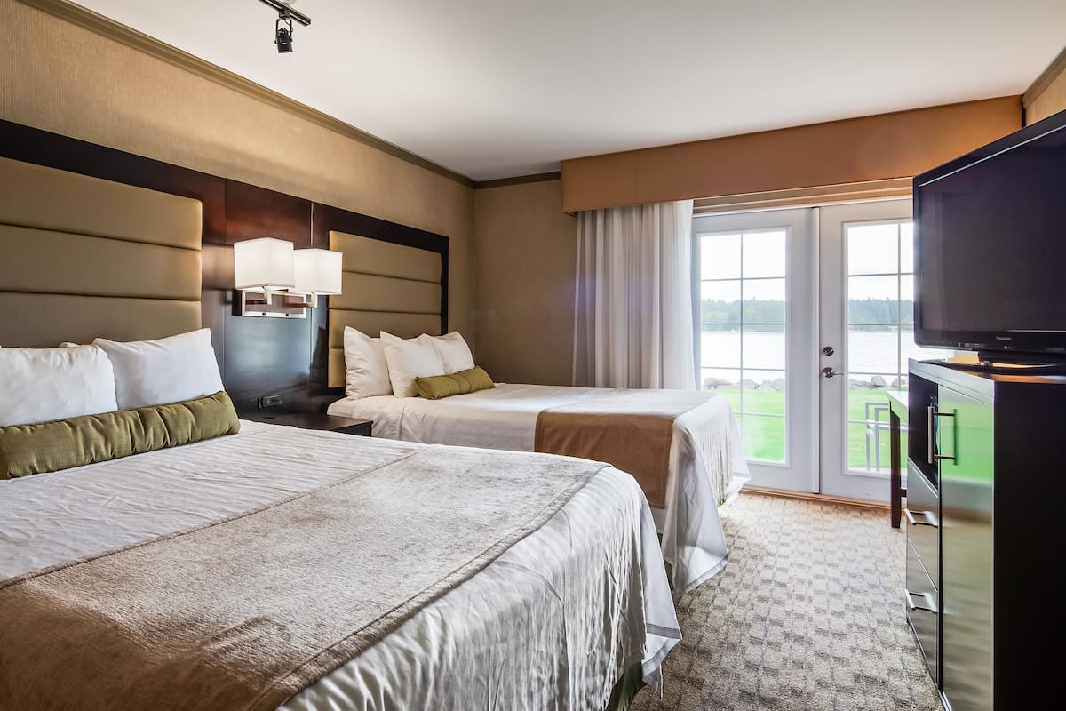 Een hotelkamer met twee bedden, een televisie en uitzicht op een waterpartij.