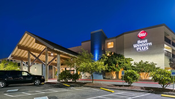 Un hotel Best Western Plus con entrada techada, estacionamiento y un edificio azul destacado al fondo.