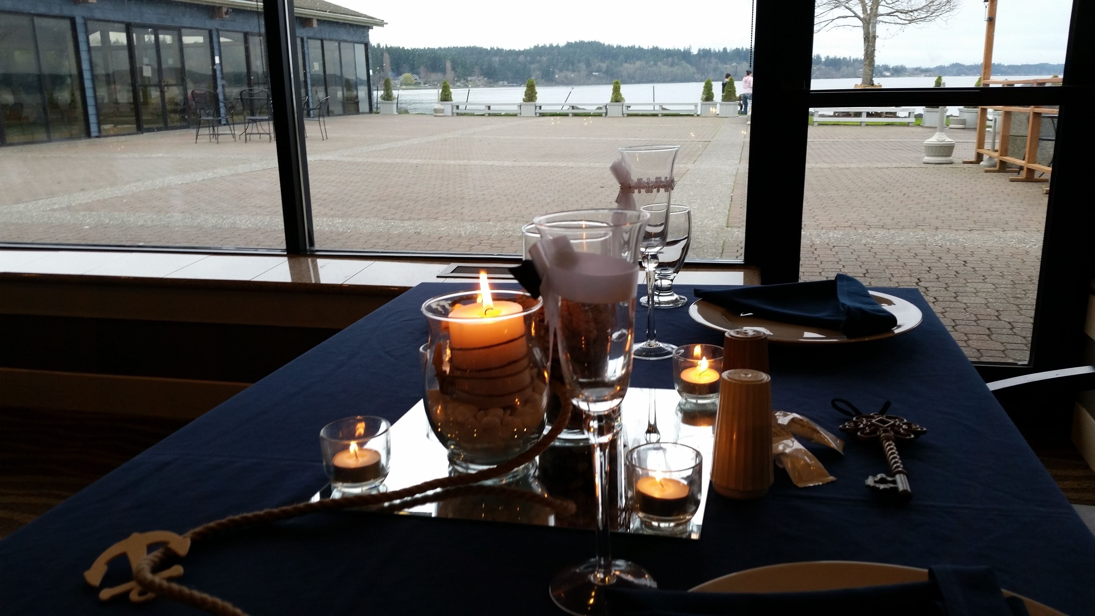 A table set with candles, glasses, and cutlery, overlooking a lakeside view.